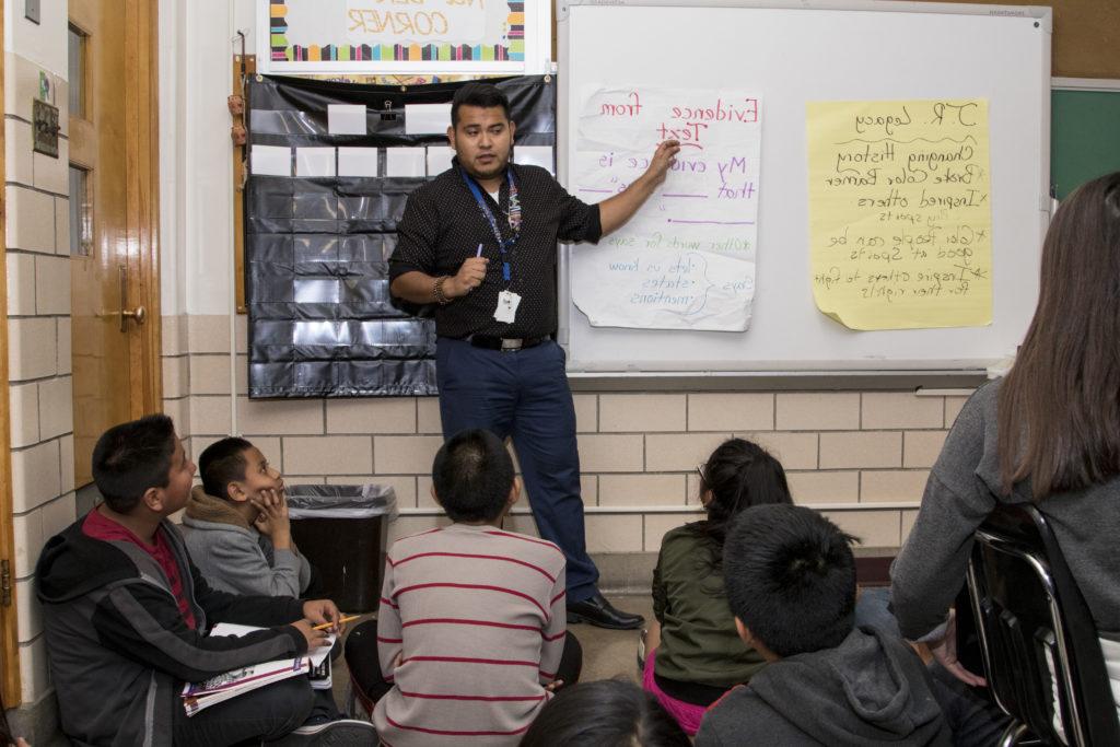 Elementary school teacher Hazael Roman Lagunas standing at the front of the class with students sitting on the floor in front of him.