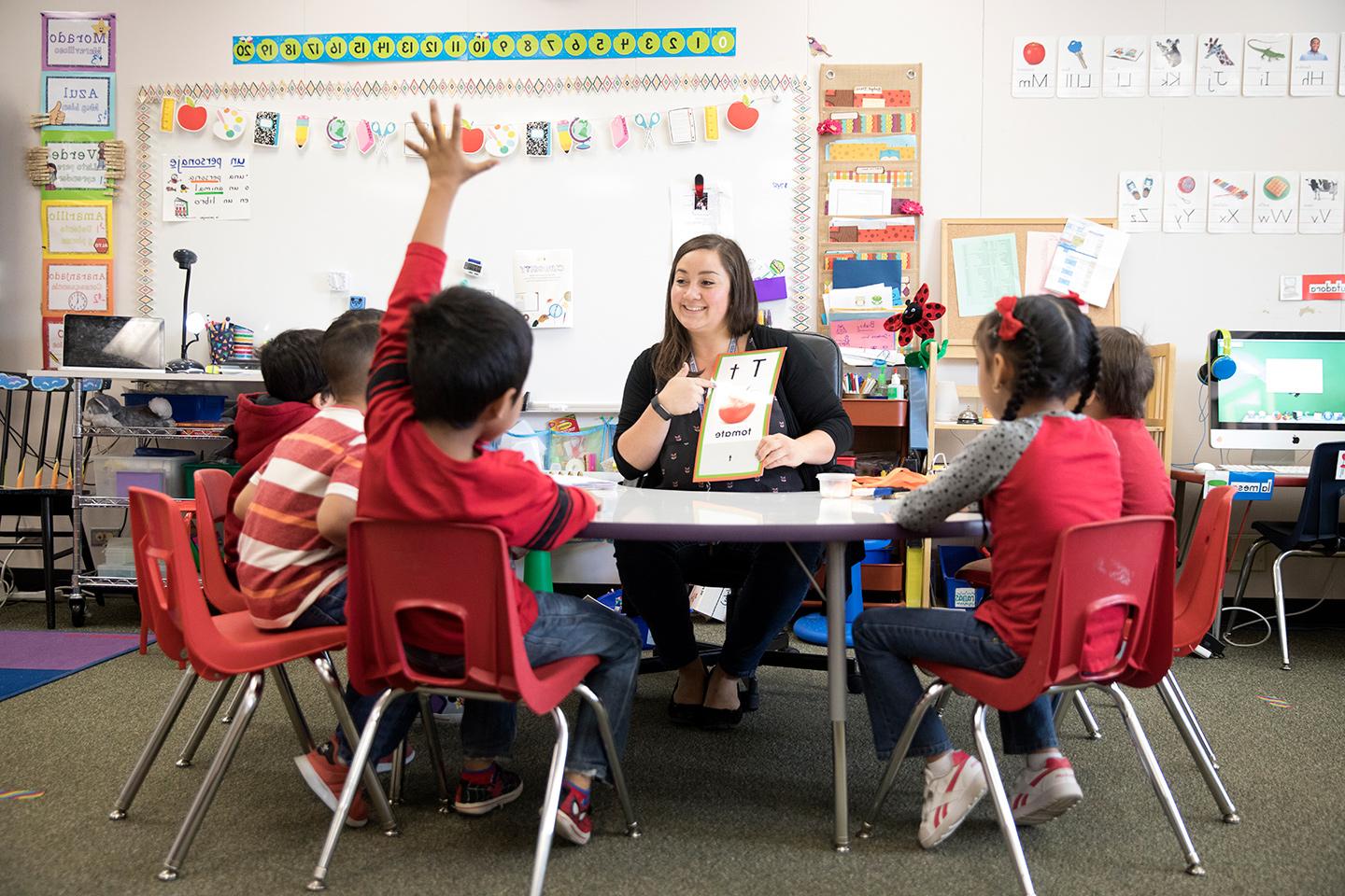 Elementary teacher Jacqueline Lujan sitting at a table in a classroom with children