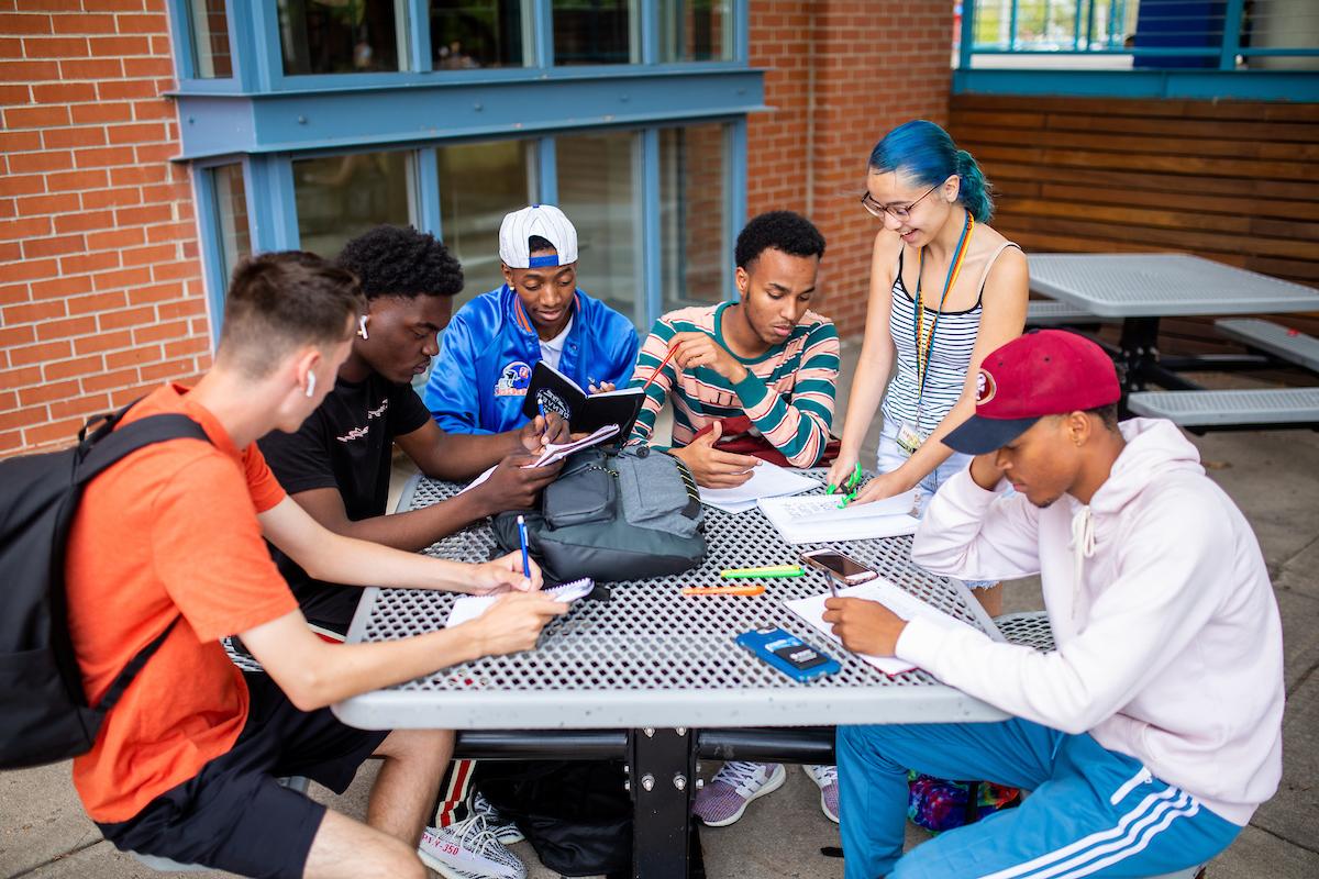六名学生在蒂沃利学生会外的桌子上拿着笔记本学习