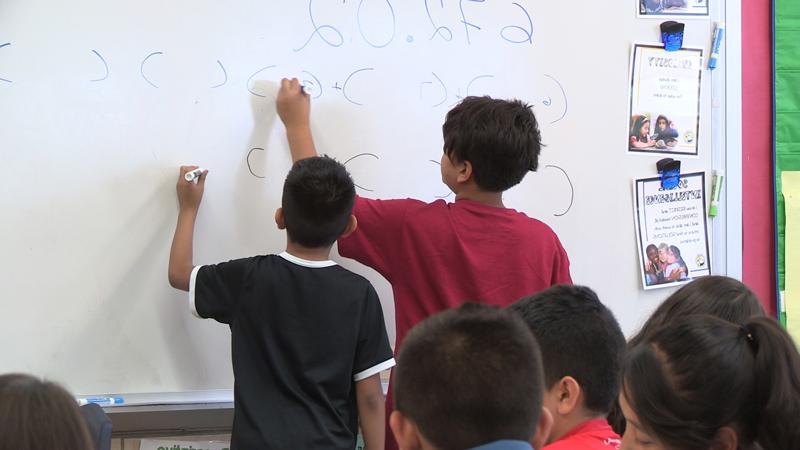 两个小学生站在白板前解数学方程式的画面.