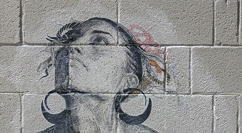 A concrete block wall with an image wheat pasted to it of a woman looking towards the sky