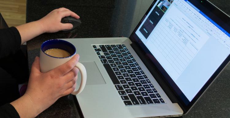 一个女人拿着咖啡在笔记本电脑上工作的特写.