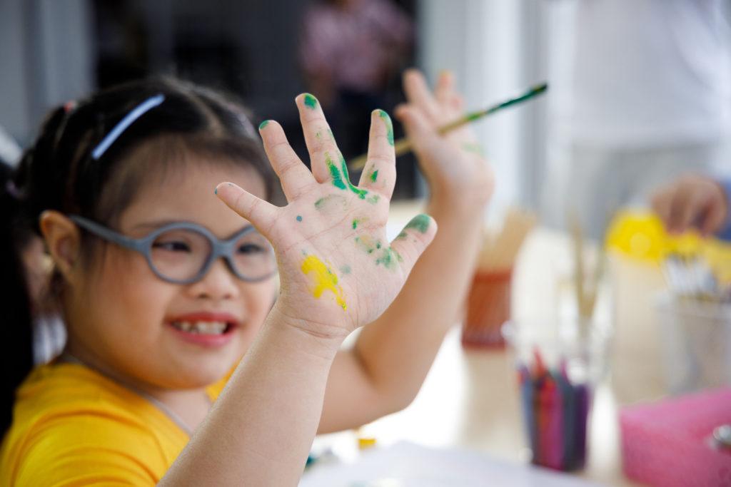 快乐的患有唐氏综合症的亚洲女孩在美术课上用水彩画了手.