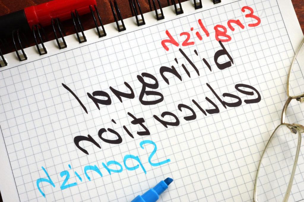 笔记本上一张格子纸的照片，上面写着“英语”, 双语教育, 用红色写的西班牙语, 黑色和蓝色记号笔.
