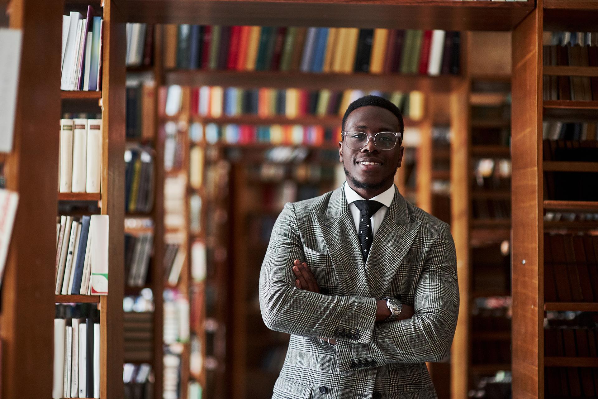 一个穿着西装的非裔美国人站在阅览室的图书馆里.