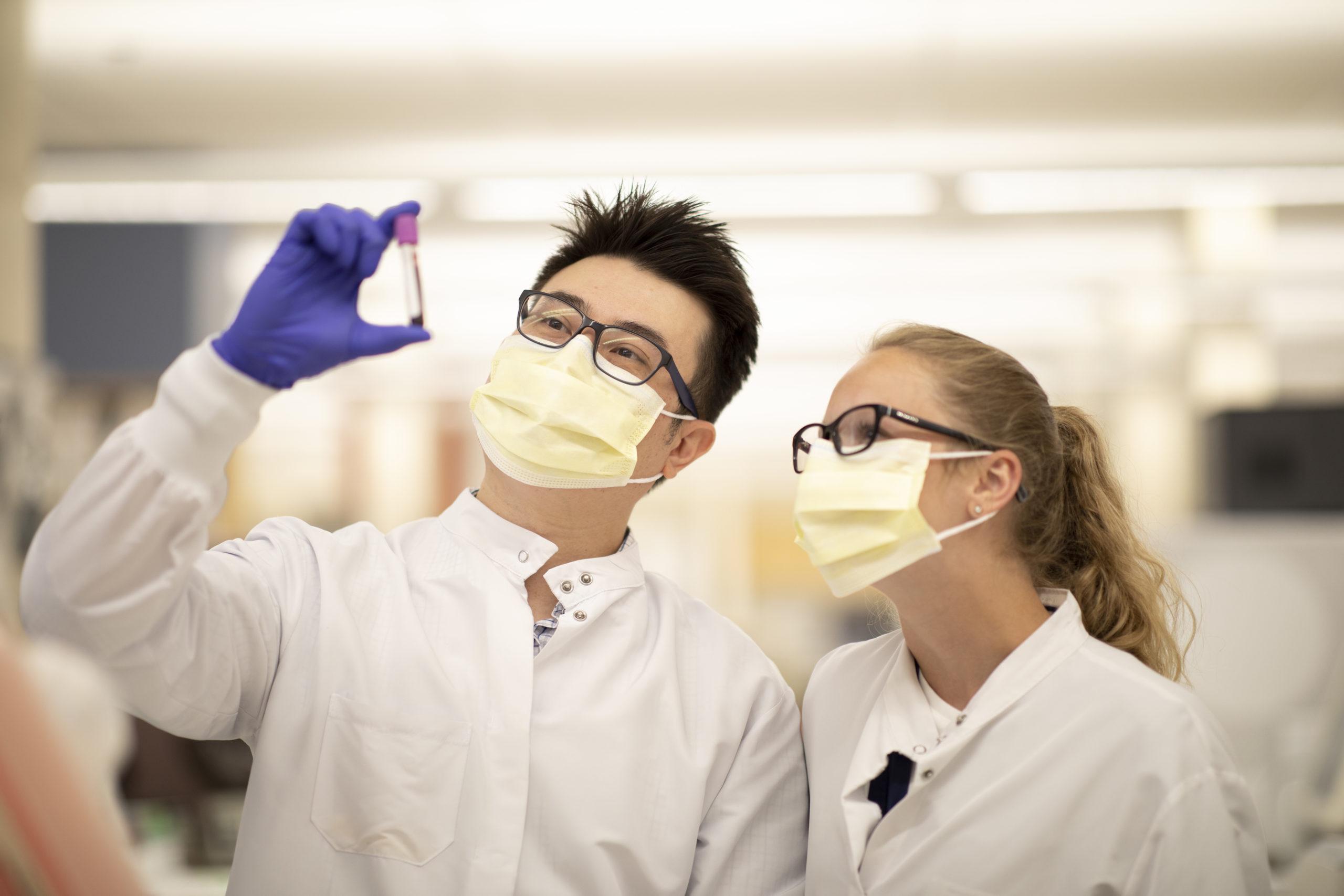 两个穿着实验室工作服，戴着口罩的人正在检查试管样本.