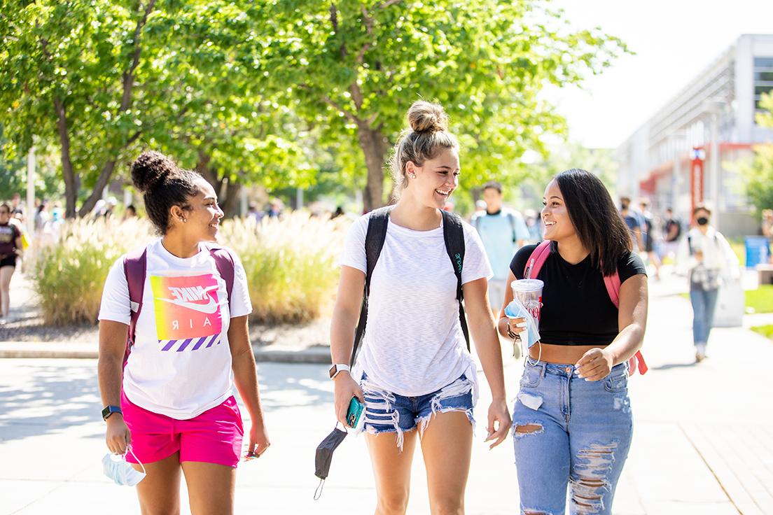 三个学生走向观众，穿过绿色和阳光明媚的Auraria校园
